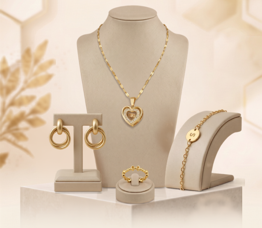 Gold jewelry set displayed on beige jewelry stands, including a heart pendant necklace, hoop earrings, a bracelet, and a ring, with the text 'JEWELRY' and 'Timeless pieces, made to shine' at the top.