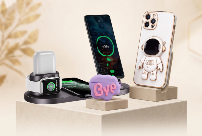 A promotional display for phone accessories showing a smartphone, an Apple Watch, a wireless charging pad, a small pink pouch, and a phone case with an astronaut design, arranged on pedestals under the text 'PHONE ACCESSORIES'.